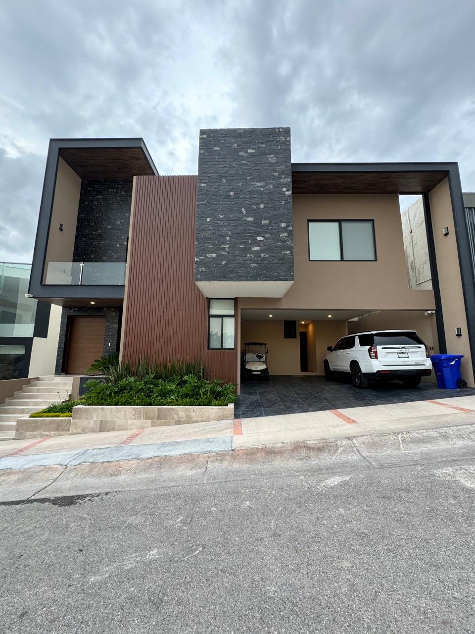 2f27cdf9-301a-4584-aba6-4afe341930fc Fachada moderna de casa en La Loma Residential & Golf Club con vistas a la ciudad y jardín iluminado.