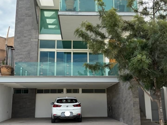 Casa moderna de tres niveles en Pedregal 2 con fachada de piedra volcánica, amplios ventanales y cochera para 3 autos.