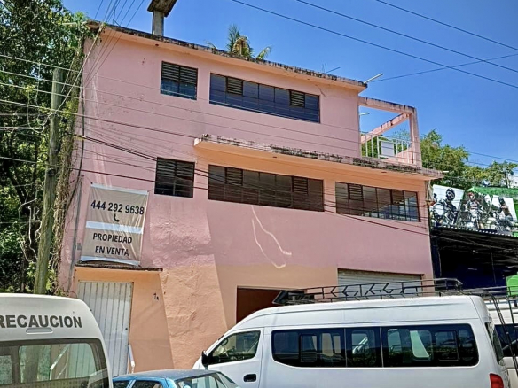 Edificio comercial de tres plantas en venta ubicado en Blvd. 20 de Noviembre, Tamazunchale, SLP. Fachada color rosa con lona de venta y ventanas amplias.